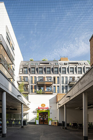 Ein Eingang mit Parkplätzen des Alnatura Marktes liegt im Innenhof des Wohnquartiers.