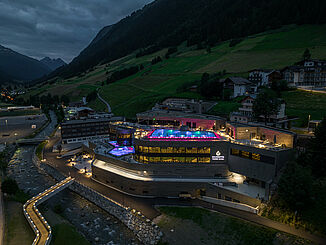 Frontansicht der beleuchteten Silvretta Therme in Ischgl bei Nacht mit umliegenden Wohngebäuden.