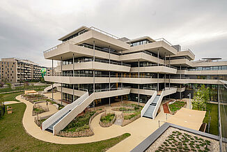 Ein Gebäudeteil des Aaron Mencer Campus in Wien mit umlaufenden Terrassen und Gartenanlage .