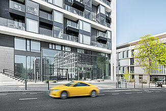 Eingangsbereich vom Henninger Turm in Frankfurt mit einem gelben vorbeifahrenden Auto.