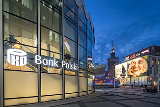 Die bleuchtete Bank Polski im Mixed-Use Gebäude Rotunda und weitere Geschäftshäuser in Warschau bei Nacht.