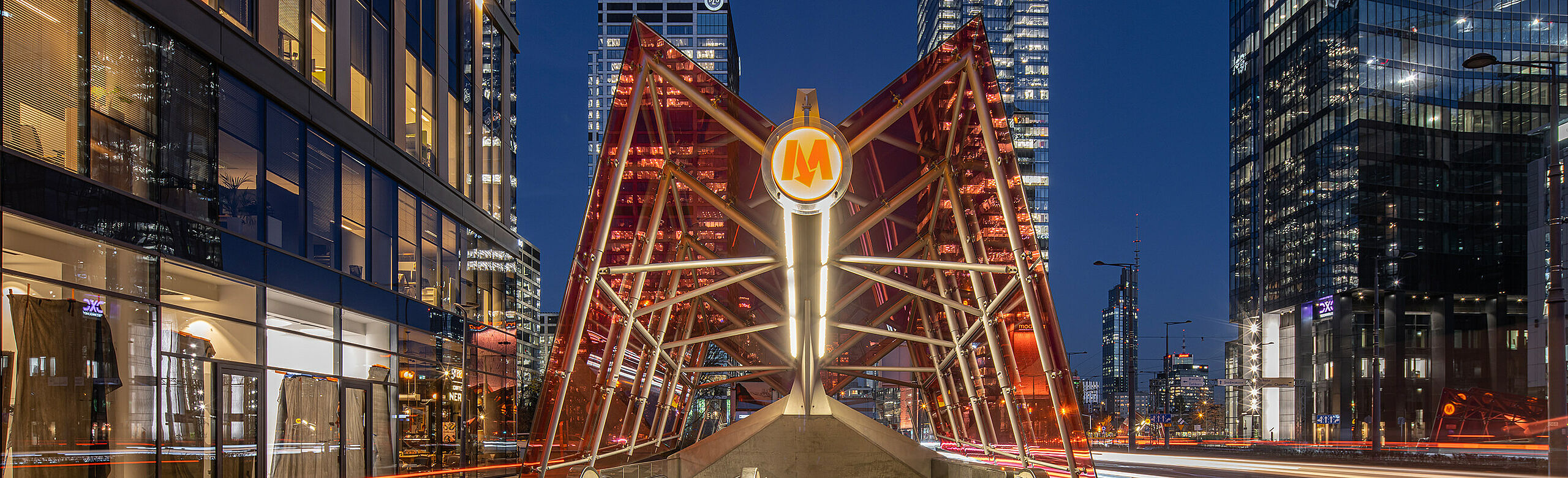 Warsaw at night with illuminated metro access and commercial buildings.