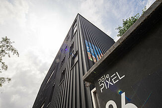 Schwarze Fassade mit Reklame und Fenstern an einem Gebäude vom Büro- und Geschäftsgebäude Pôle PIXEL in Frankreich.