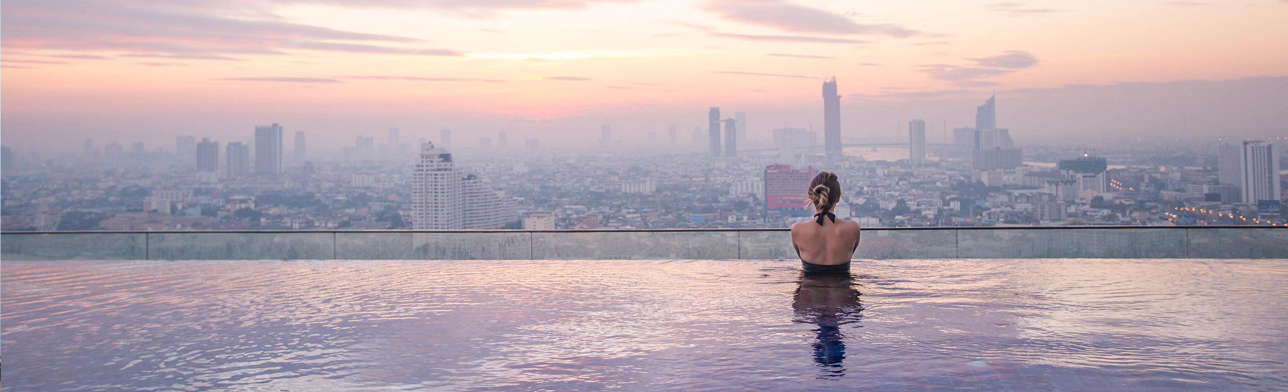 Eine Frau steht in einem Infinitypool und schaut sich die Skyline der Stadt an.