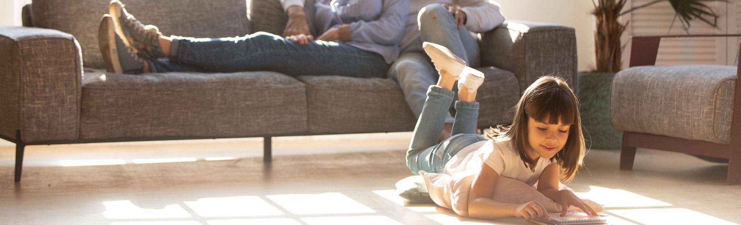 A girl lies on a wooden floor in the living room and reads a book.